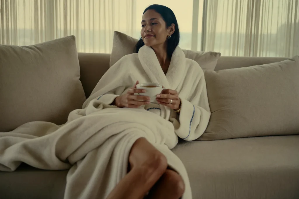 Woman resting comfortably at home during mommy makeover recovery near Newport Beach, wrapped in a soft robe with tea.